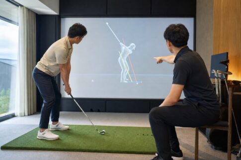 インドアゴルフスタジオでコーチとスイングデータを確認するゴルファー