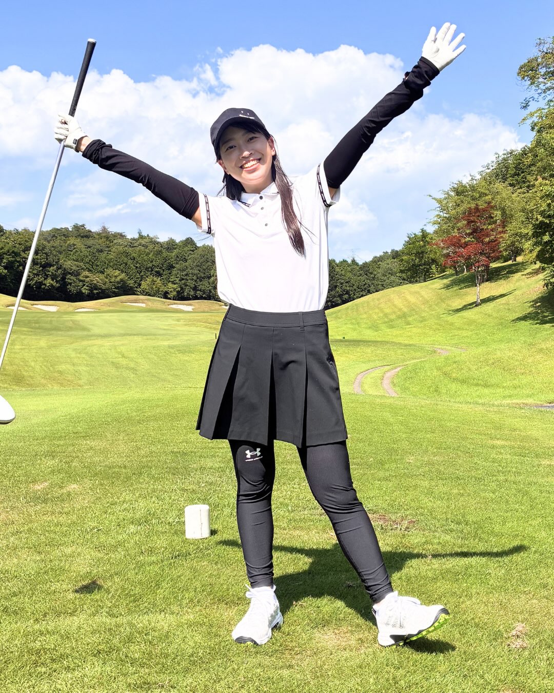 白いゴルフポロと黒いプリーツスカートを着た女性のゴルフコーデ