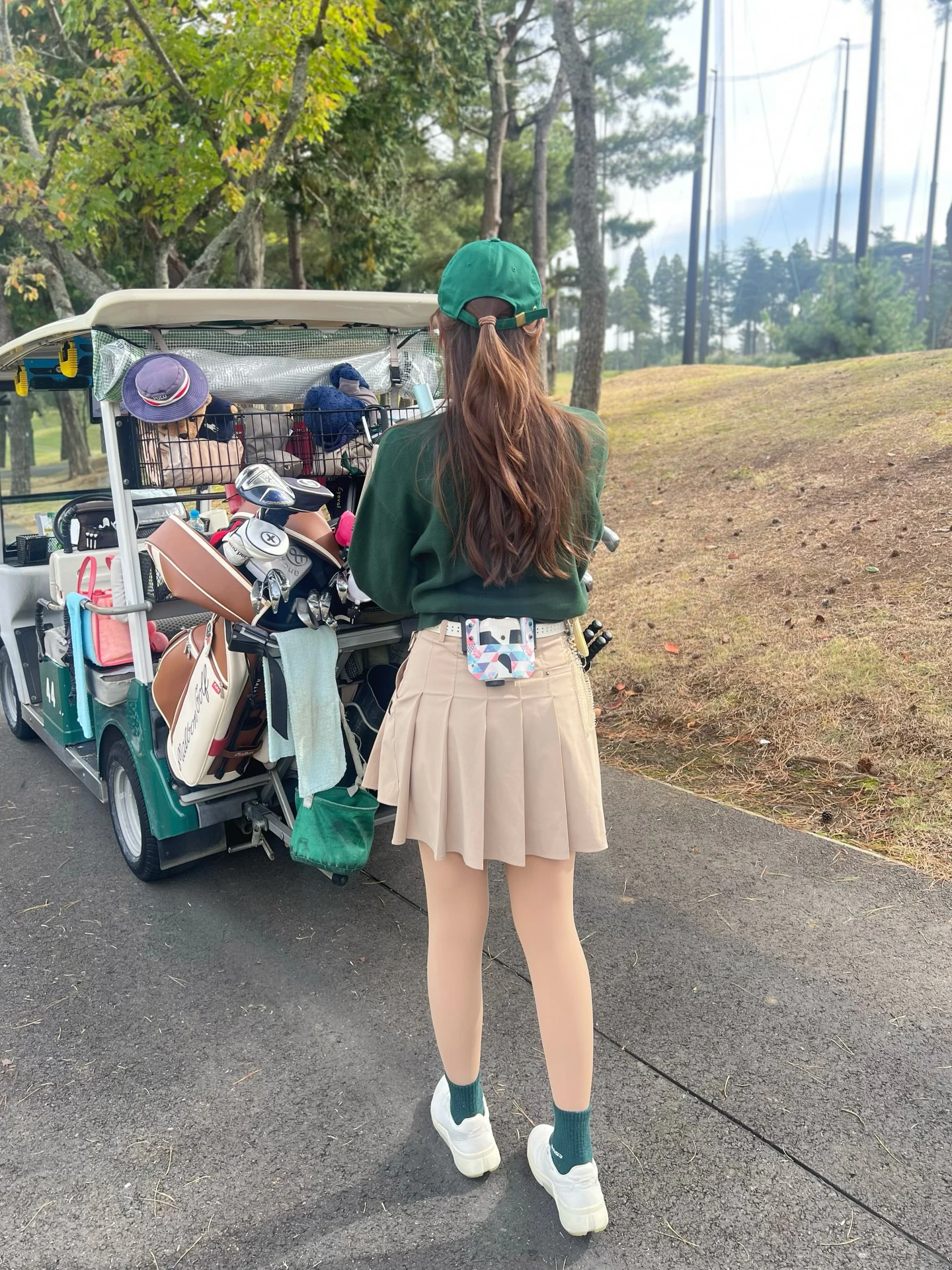 深みグリーンのトップスとベージュスカートを合わせたレディース秋ゴルフコーデ